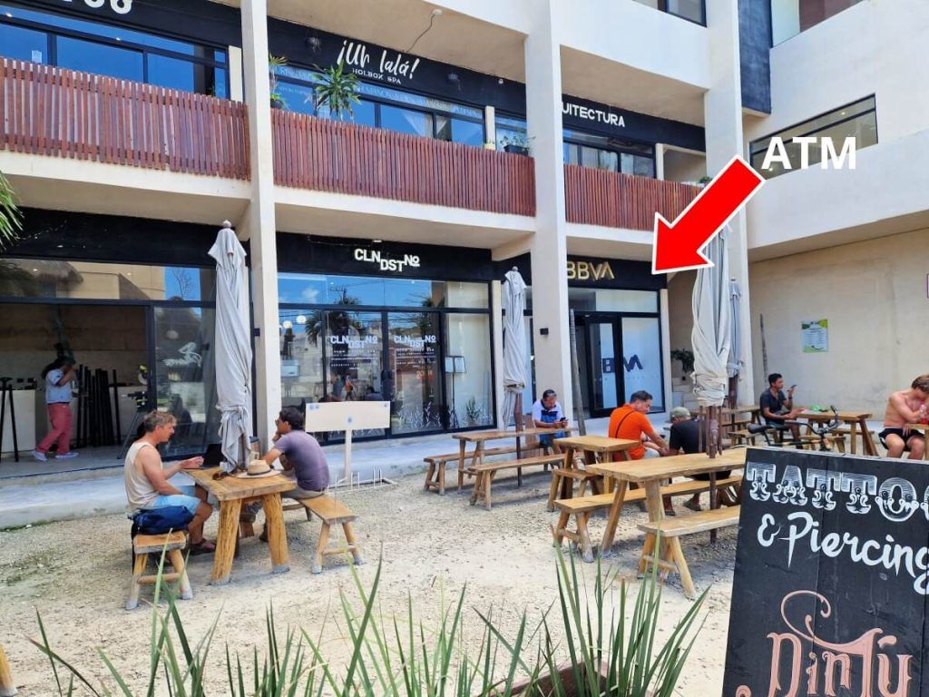 Outdoor seating area in front of a BBVA bank in Holbox with an arrow pointing to an ATM on the upper floor.