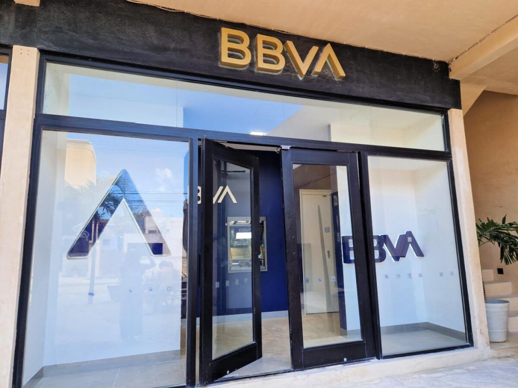 Entrance of a BBVA bank branch in Holbox with clear glass doors and a visible ATM inside.
