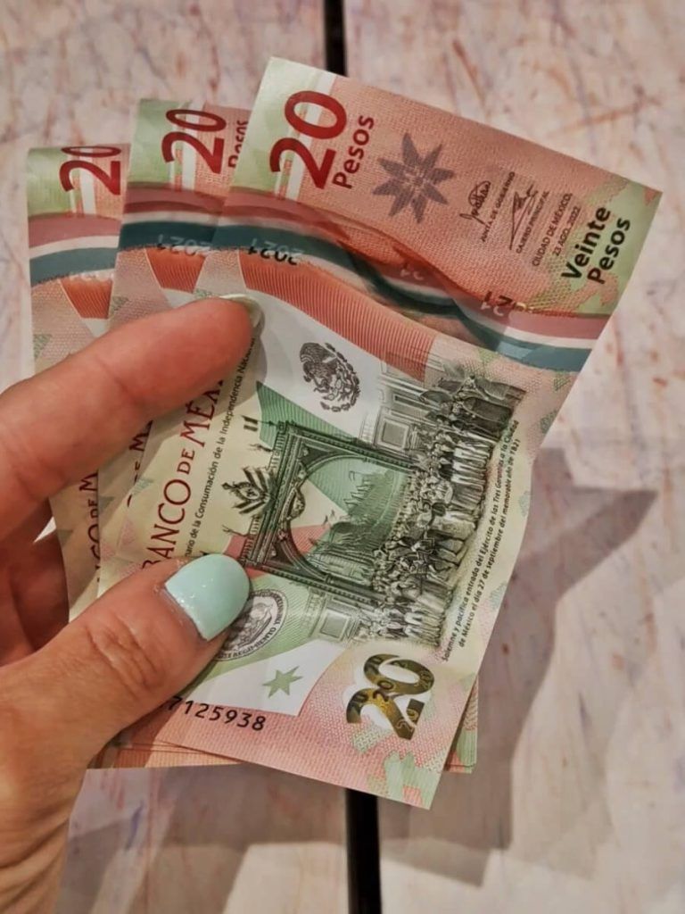 Sara's hand holding Mexican 20-peso bills, showcasing the currency's colorful design, at a vendor setting in Holbox, where local currency is preferred for cash transactions.