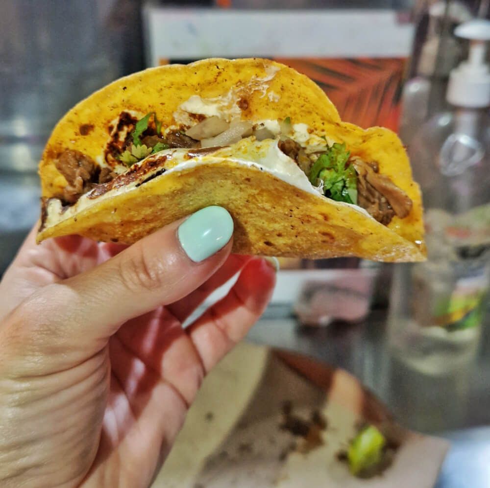 Sara's hand holding a taco quesabirria, a traditional Mexican dish, from a taco cart in Holbox; tipping at taco carts is not mandatory but is appreciated for good service.