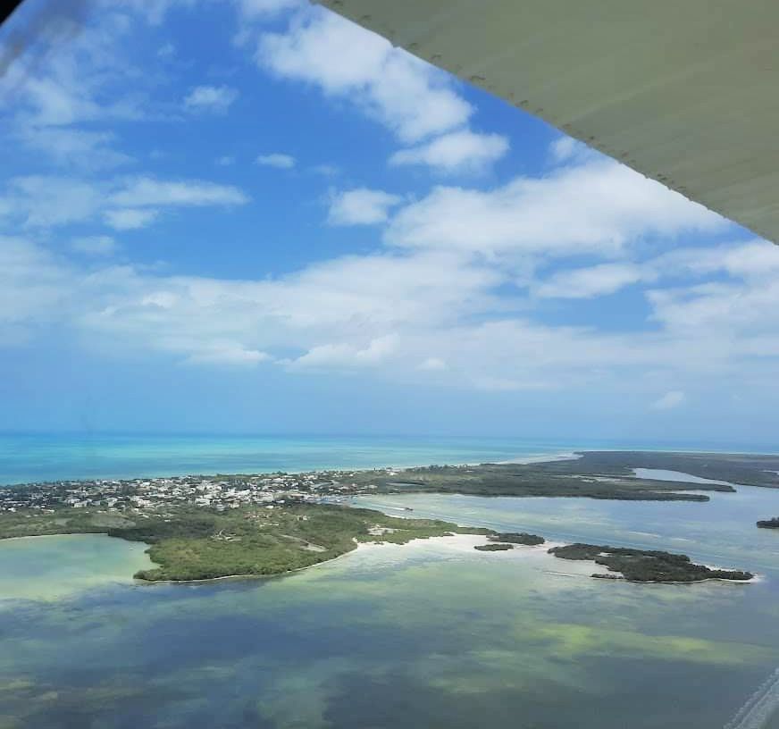 Aerial view of Holbox Island showcasing the contrast between the blue waters, patches of greenery, and the buildings of Holbox town. Part of the plane's interior is visible in the upper frame, offering a traveler's perspective.