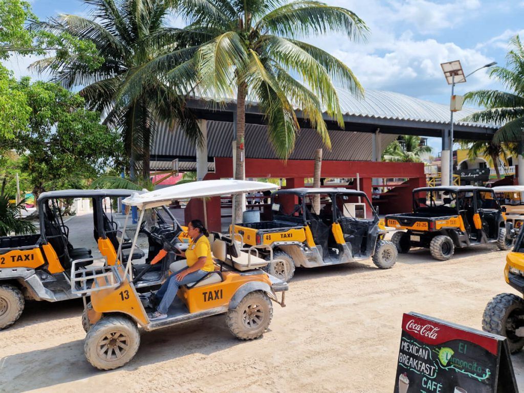 Row of golf cart taxis with distinctive yellow markings waiting for passengers next to the main square in Holbox.