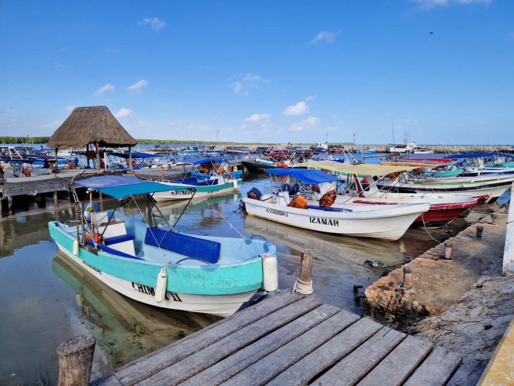 Numerous boats moored at Chiquila port with a palapa roof structure in the background and a clear blue sky above.